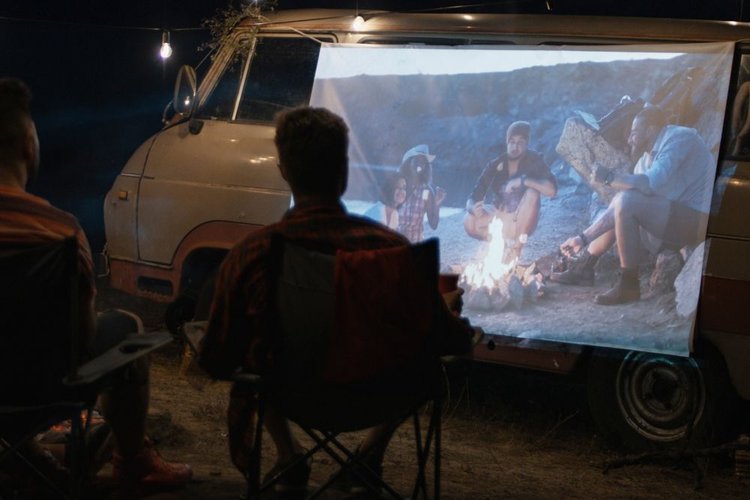 friends use a white sheet as a projector screen to watch movies in campsite