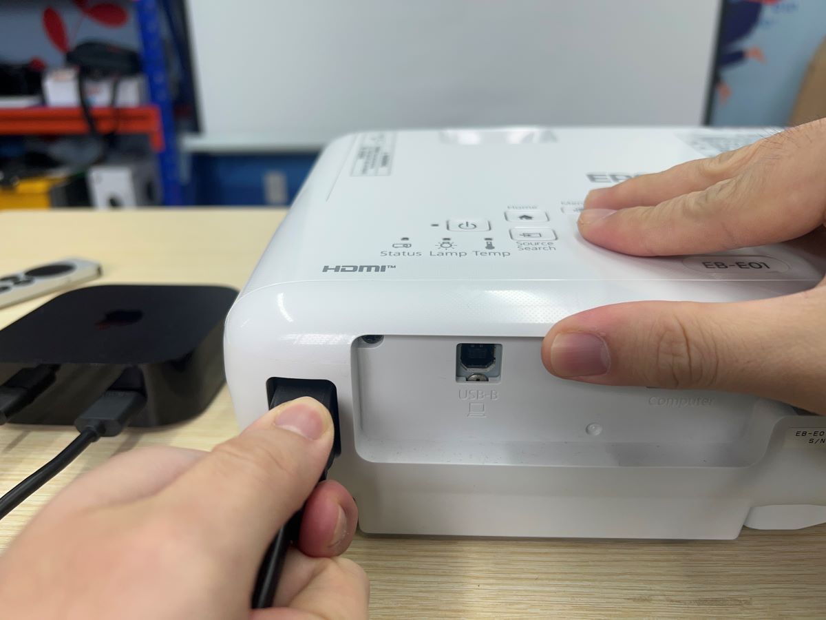 Hands are connecting the power cord while installing an Epson projector.