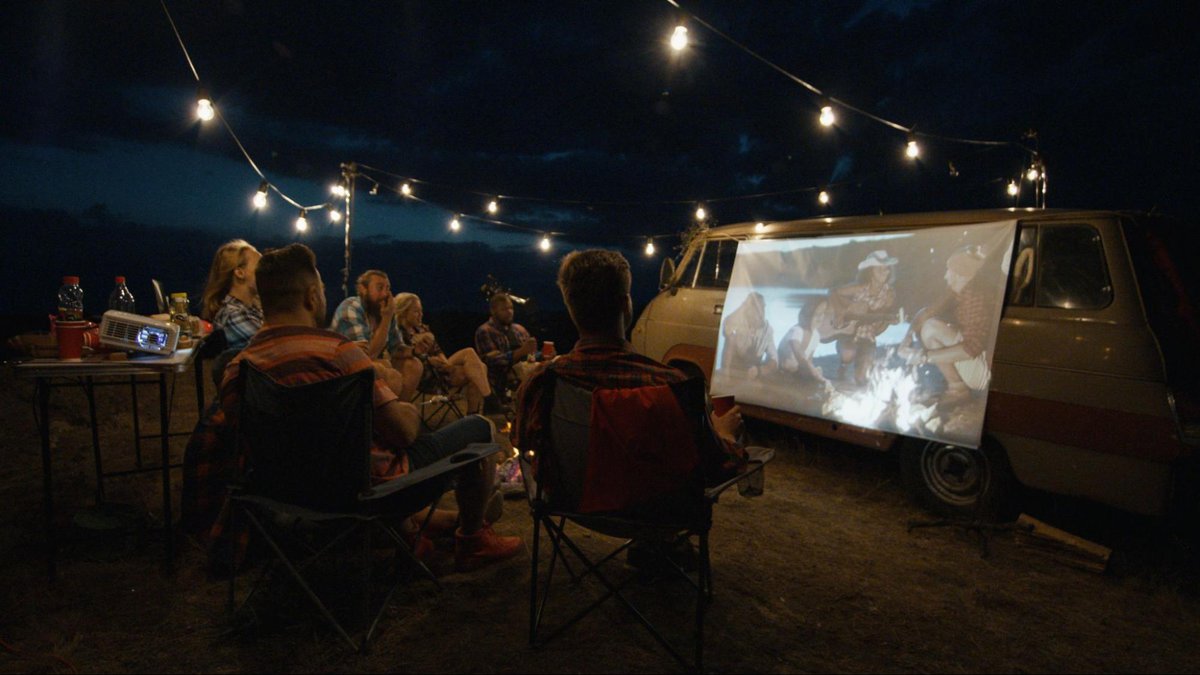a group of people is watching movies on projector screen mounted on a van