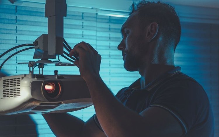 man adjusting the angle of a ceiling-mounted projector