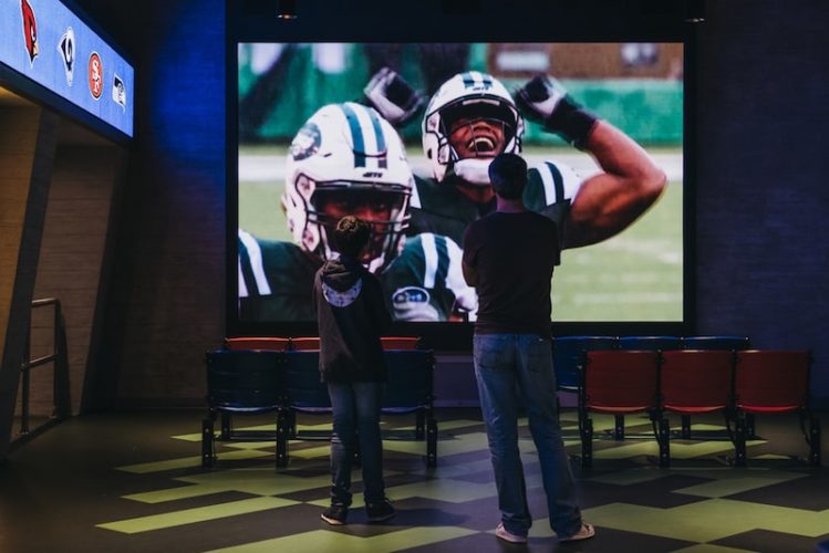 two young men are watching football on a projector screen