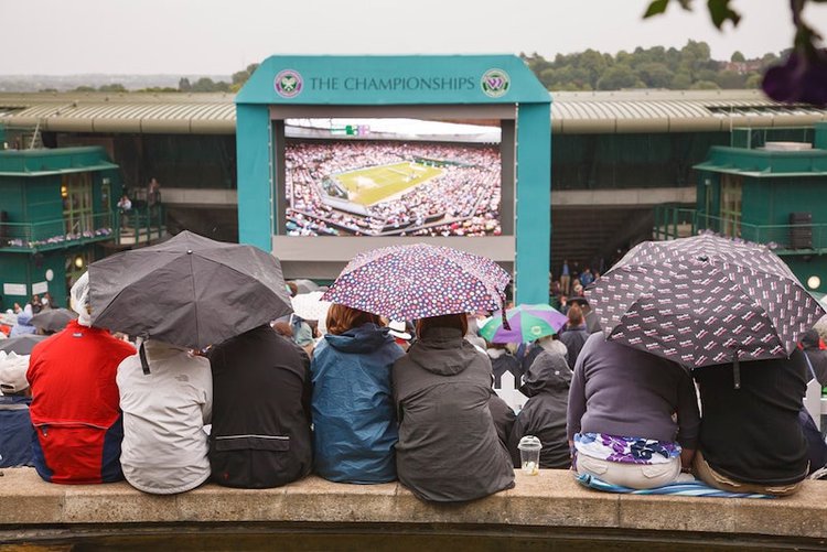 people gathering under rain watching sport on a projector screen