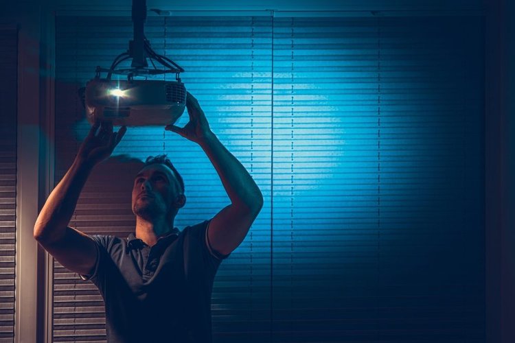A man reaching a projector on a ceiling mount