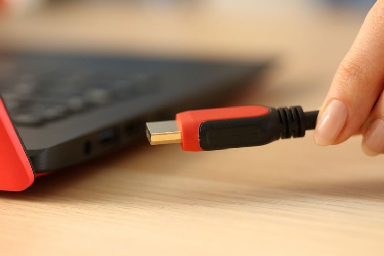 A person plug an orange hdmi cable into a laptop