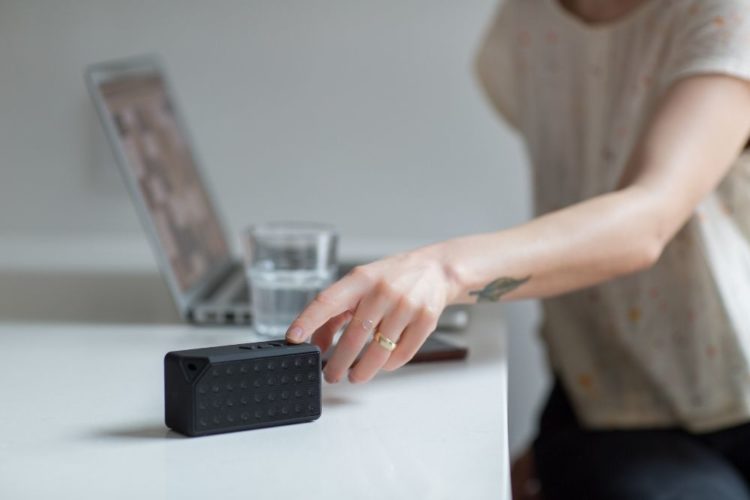 A person touching a black bluetooth speaker