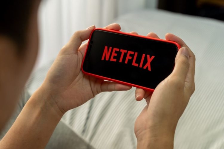 A woman is watching Netflix on a red smartphone