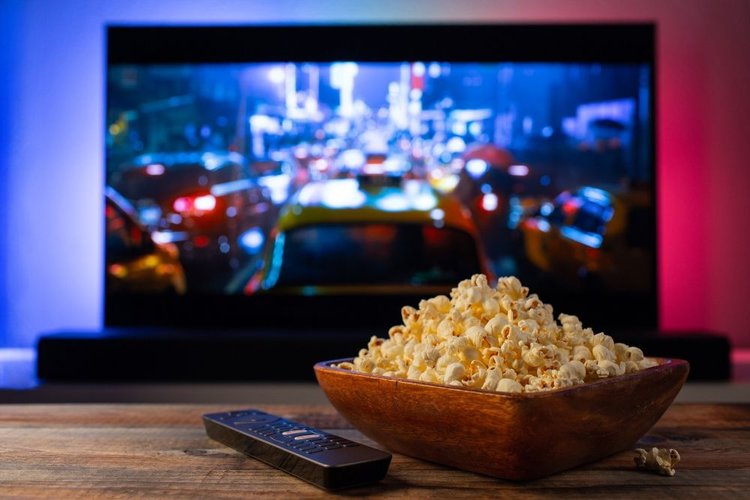 A TV playing film with remote control and popcorn