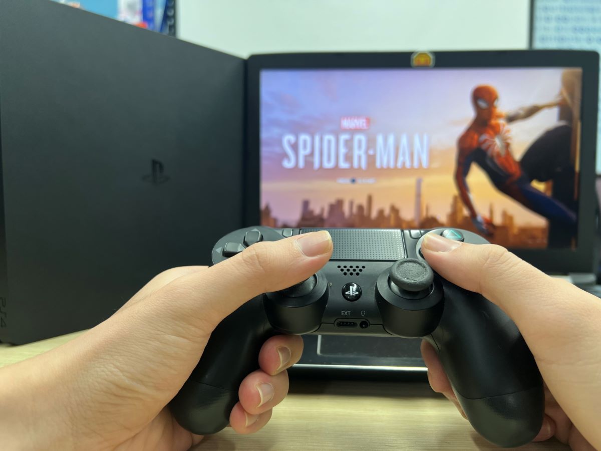 A hand is holding a PS4 controller while playing Spider-Man