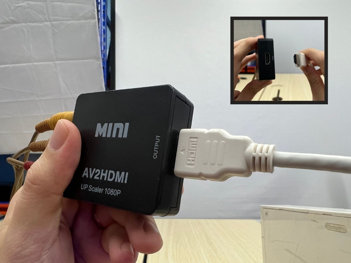 A hand is holding the RCA to HDMI adapter with an HDMI cable is plugged into the adapter