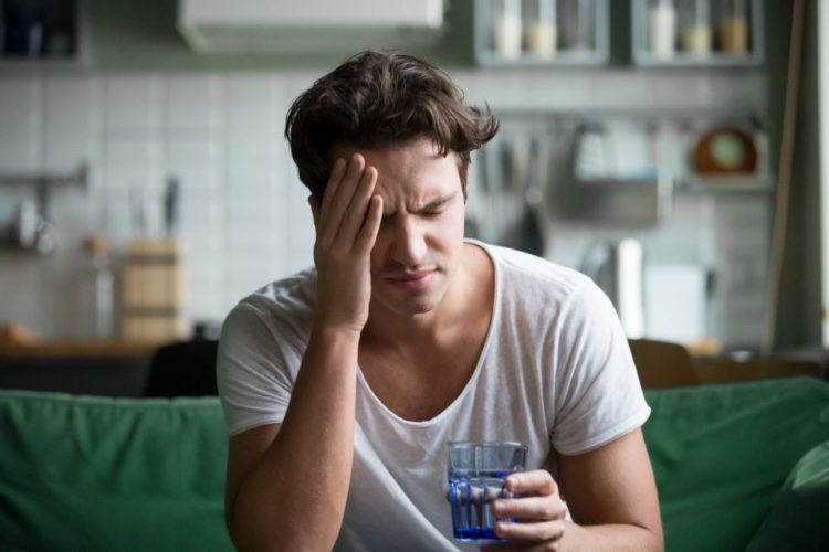 A man having a headache and holding a cup of water