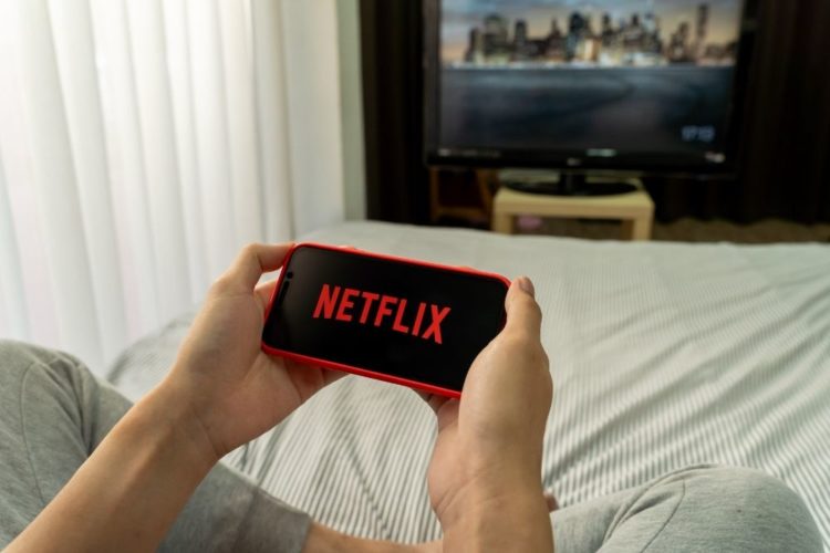 A man watching Netflix on his phone with an opening TV