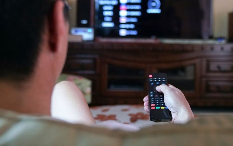 Man holds a remote control and watches TV