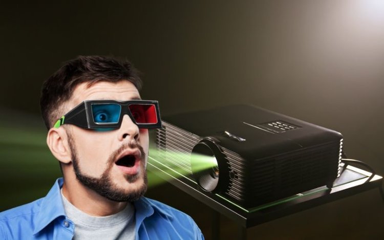 Man wearing 3D glasses beside a projector