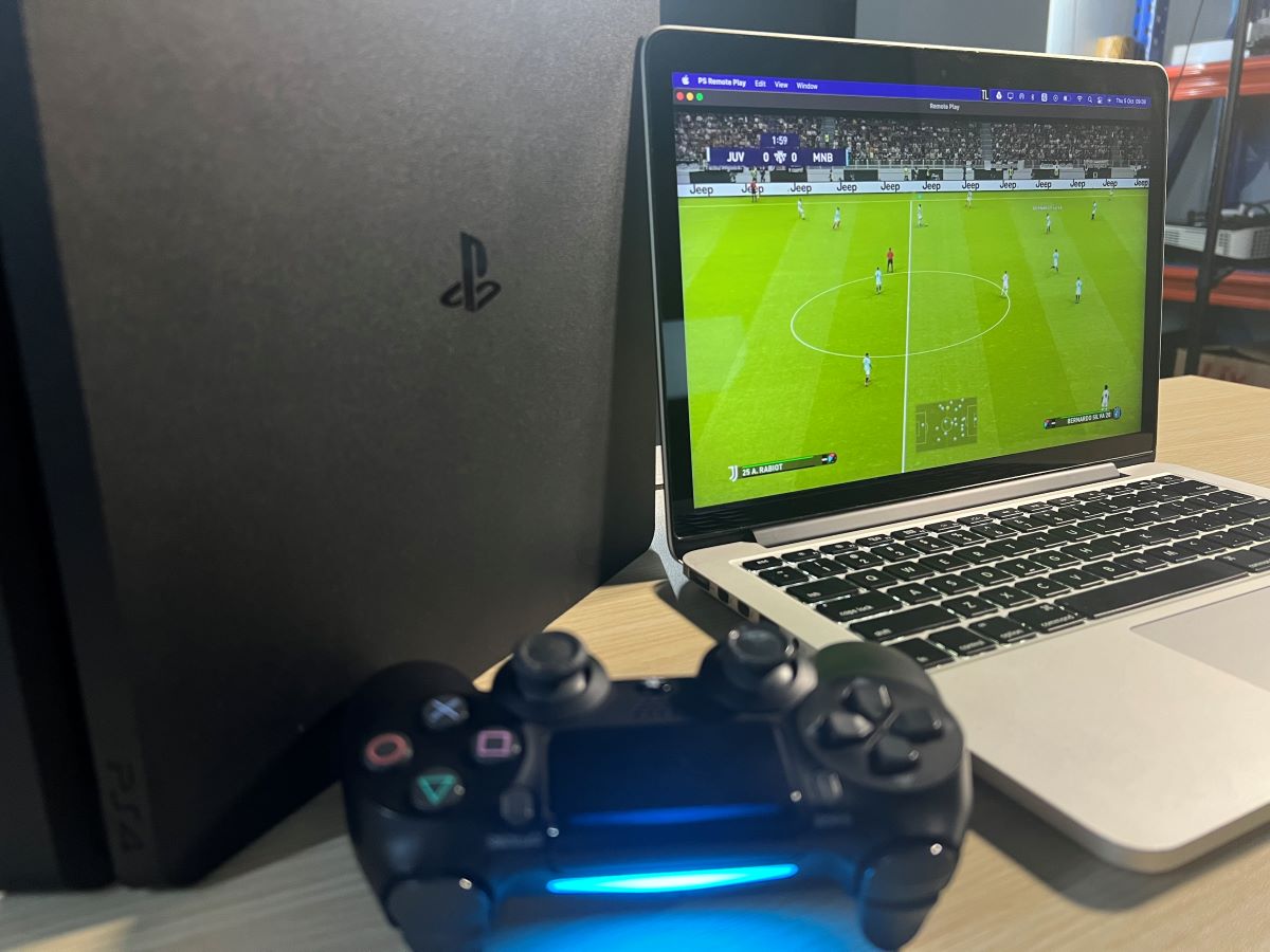 The PS4 console and controller is next to a MacBook Pro 2013 playing PES 2021