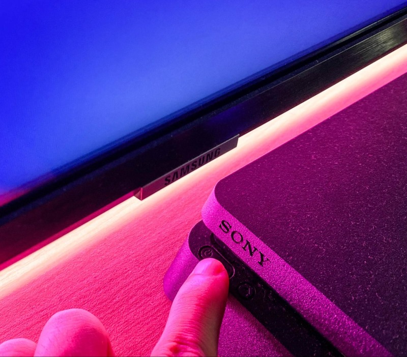 a hand is pressing the power button of a PS4 console