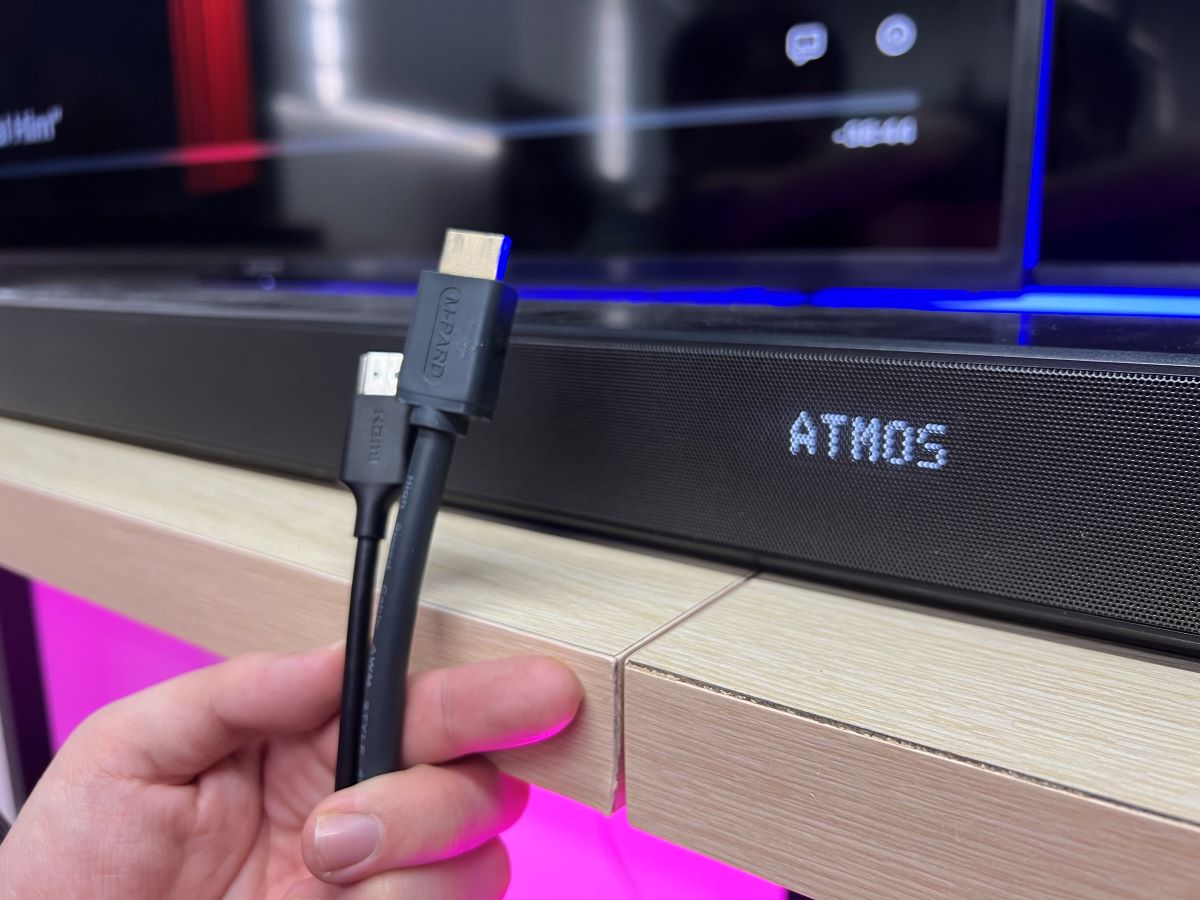 The HDMI cables are holding by a hand with a soundbar displaying Atmos mode