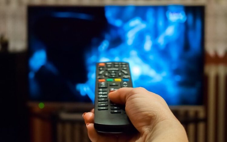 Woman hand holding TV remote in front of TV screen