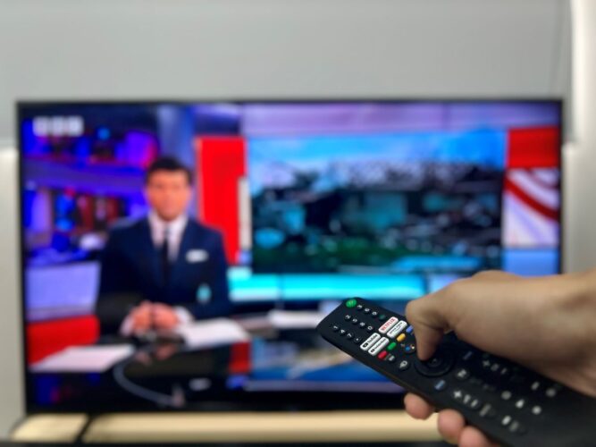 a hand holding the remote in front of the TV