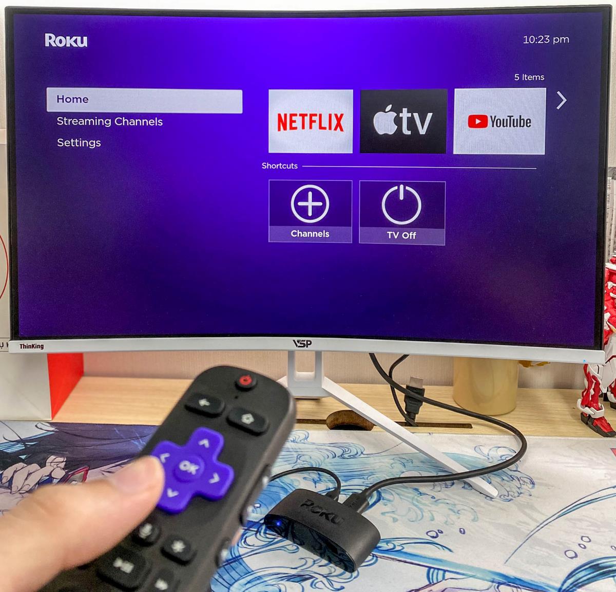 a hand is holding a Roku remote in front of a Roku screen on a monitor