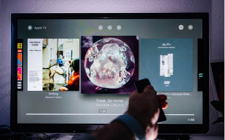 Hand holding an Apple TV remote in front of a TV