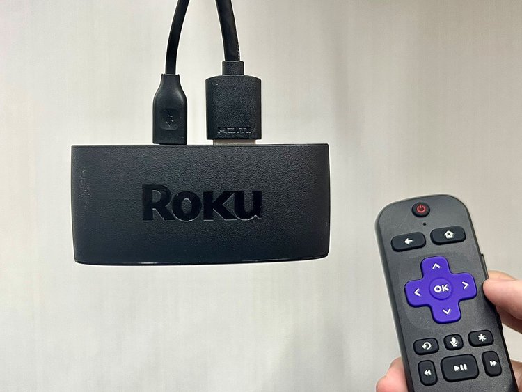 a hand holding a roku remote and a roku express 4k+ next to it