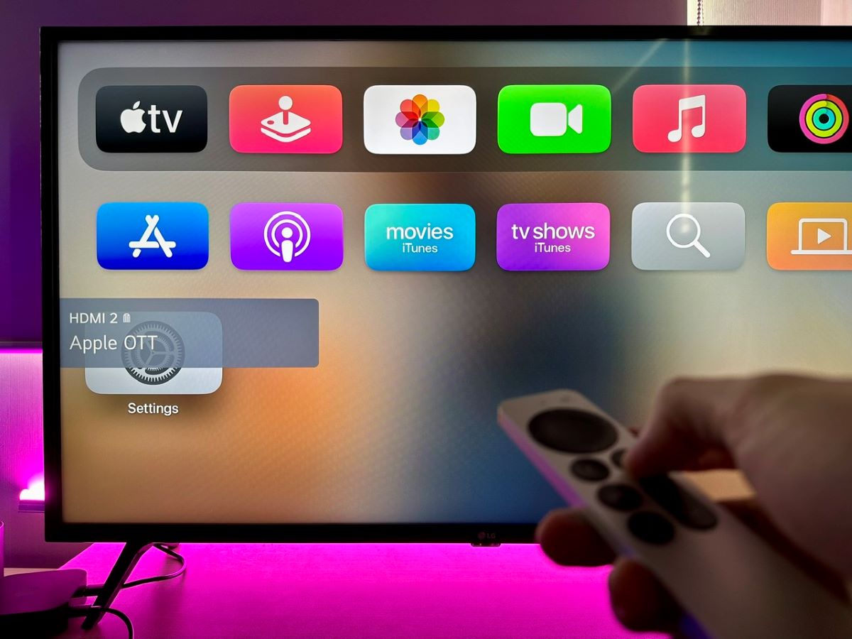 a hand holding an apple tv remote pointing at an lg tv