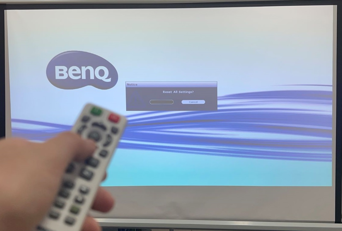 A hand is holding BenQ remote and trying to reset the projector settings