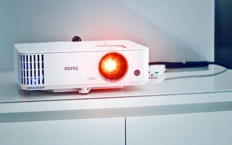 A white BenQ projector is shining with the yellow light