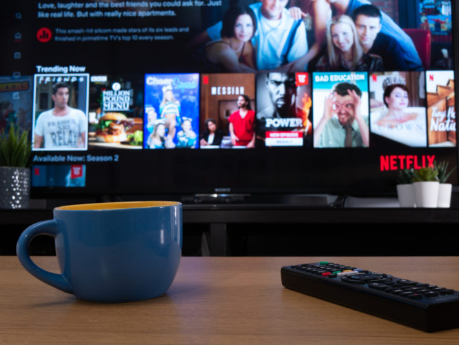 Netflix on TV with remote and cup on a table