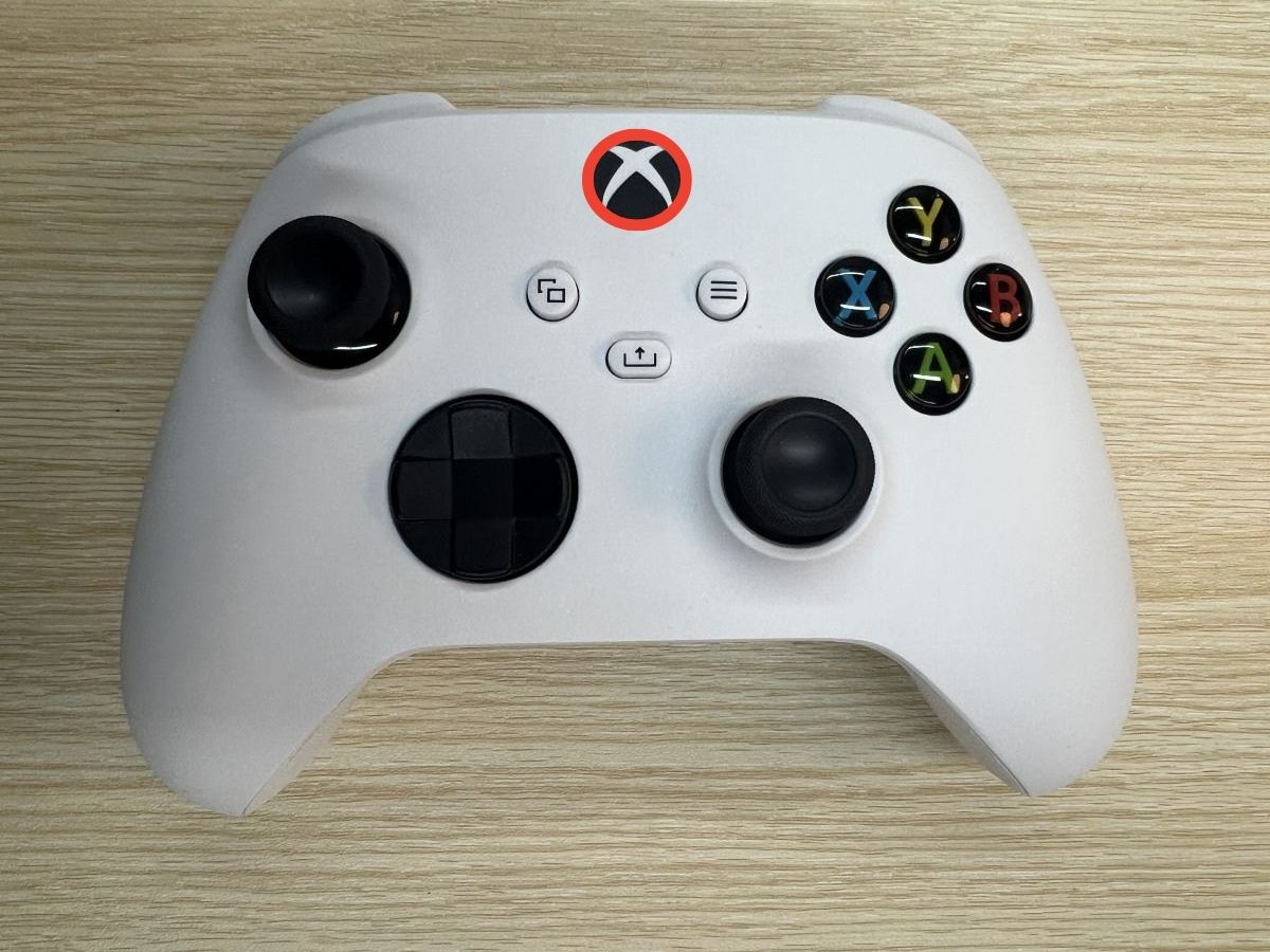 Xbox controller on a woodedn table with the Xbox button is being highlighted with a red circle