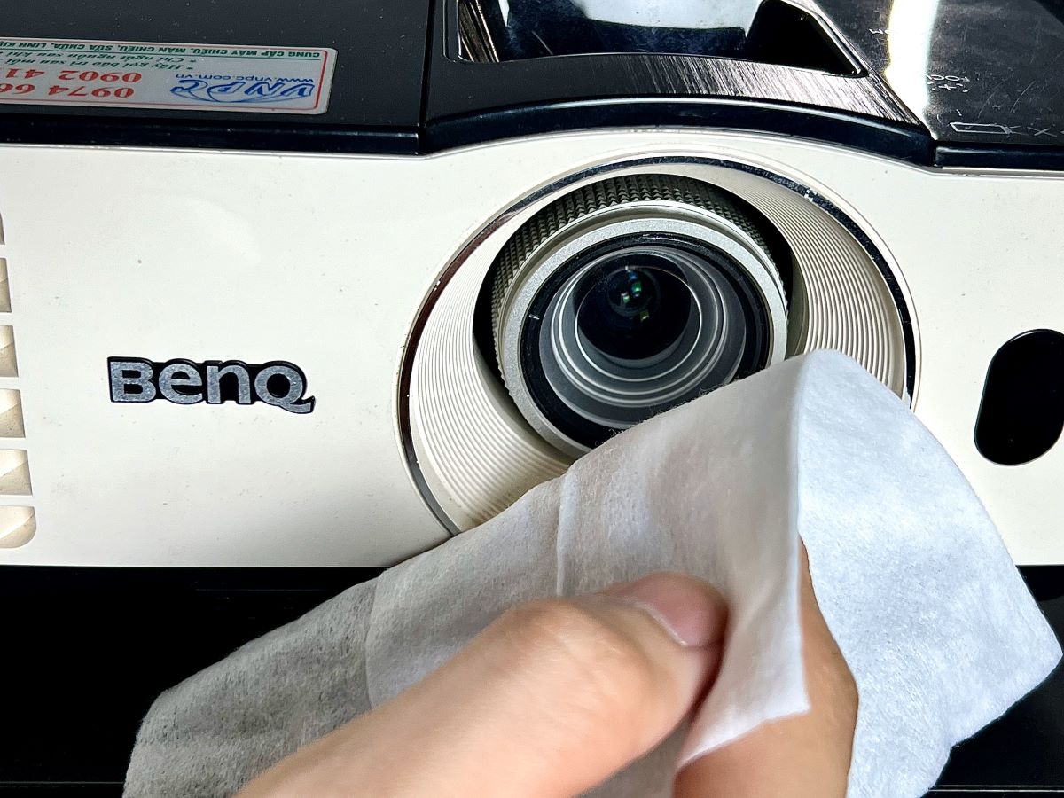 a hand holding a cloth to clean the benq projector's lens
