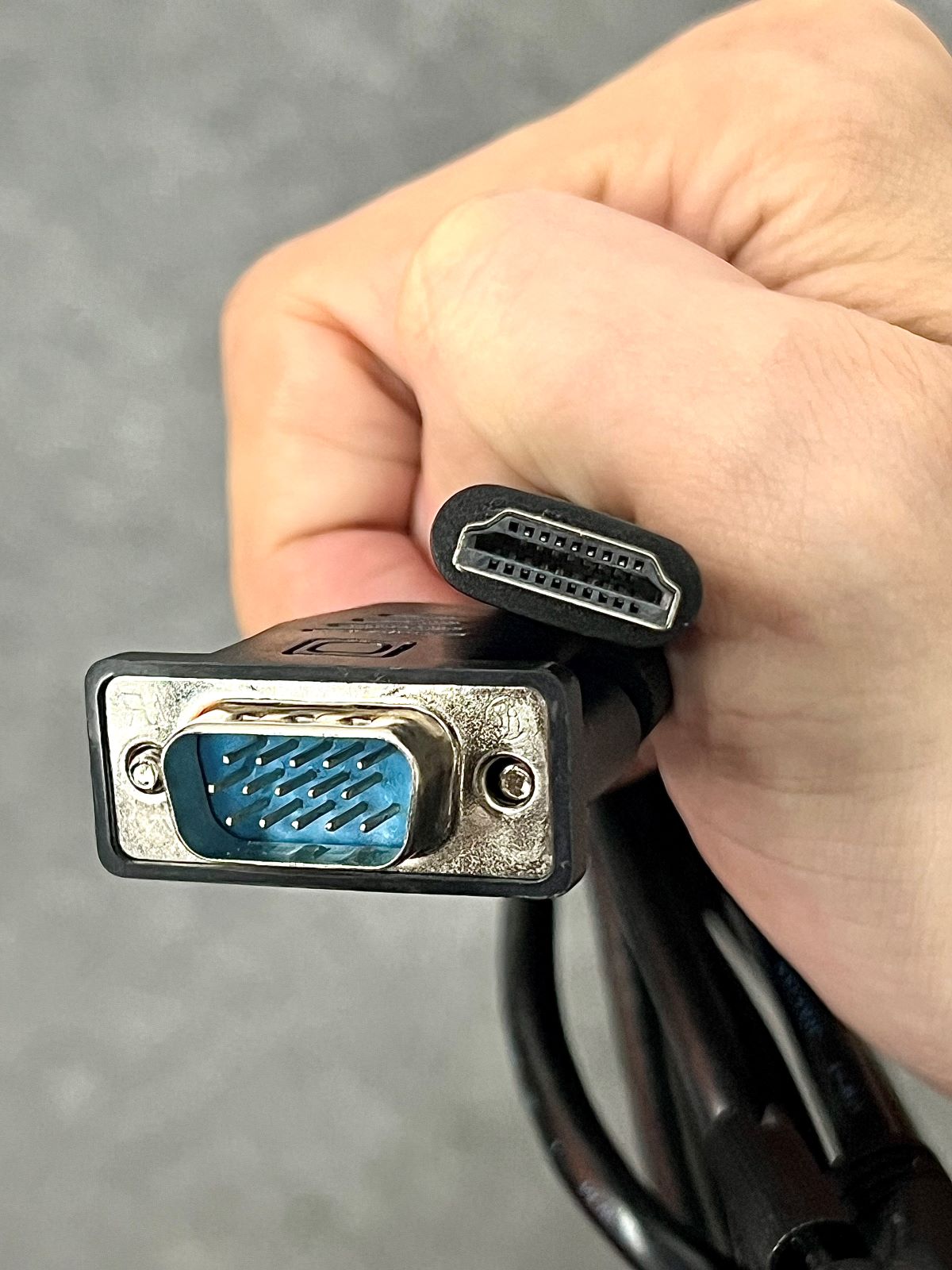 a hand holding a vga cable and an hdmi cable
