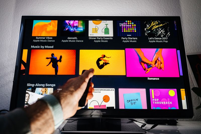 man holding Apple TV remote in front of TV