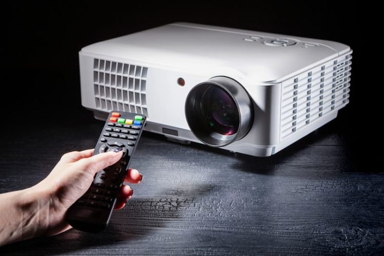 man holding a projector remote with a projector beside