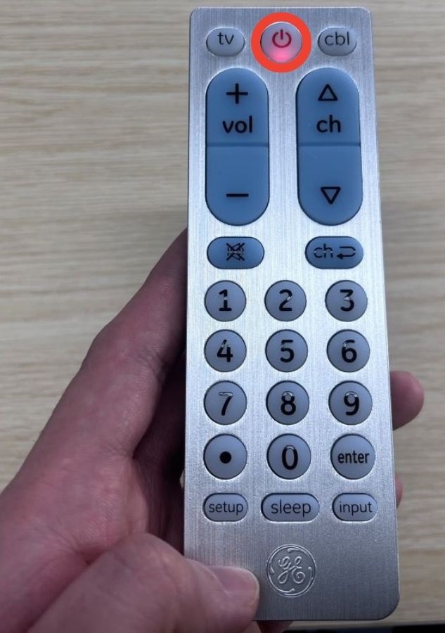 A hand is holding the GE uniseral remote with the LED light is red highlighted