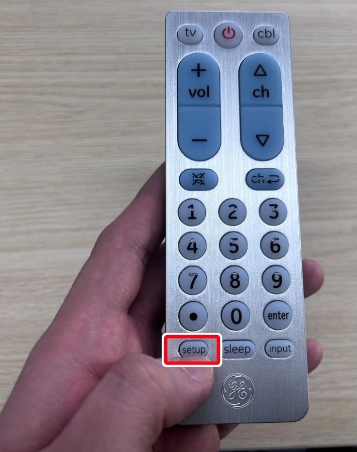 A hand is pressing the setup button on GE universal remote