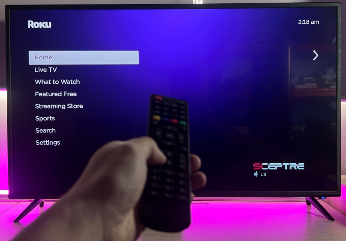 A hand is using Magnavox universal remote on Sceptre TV