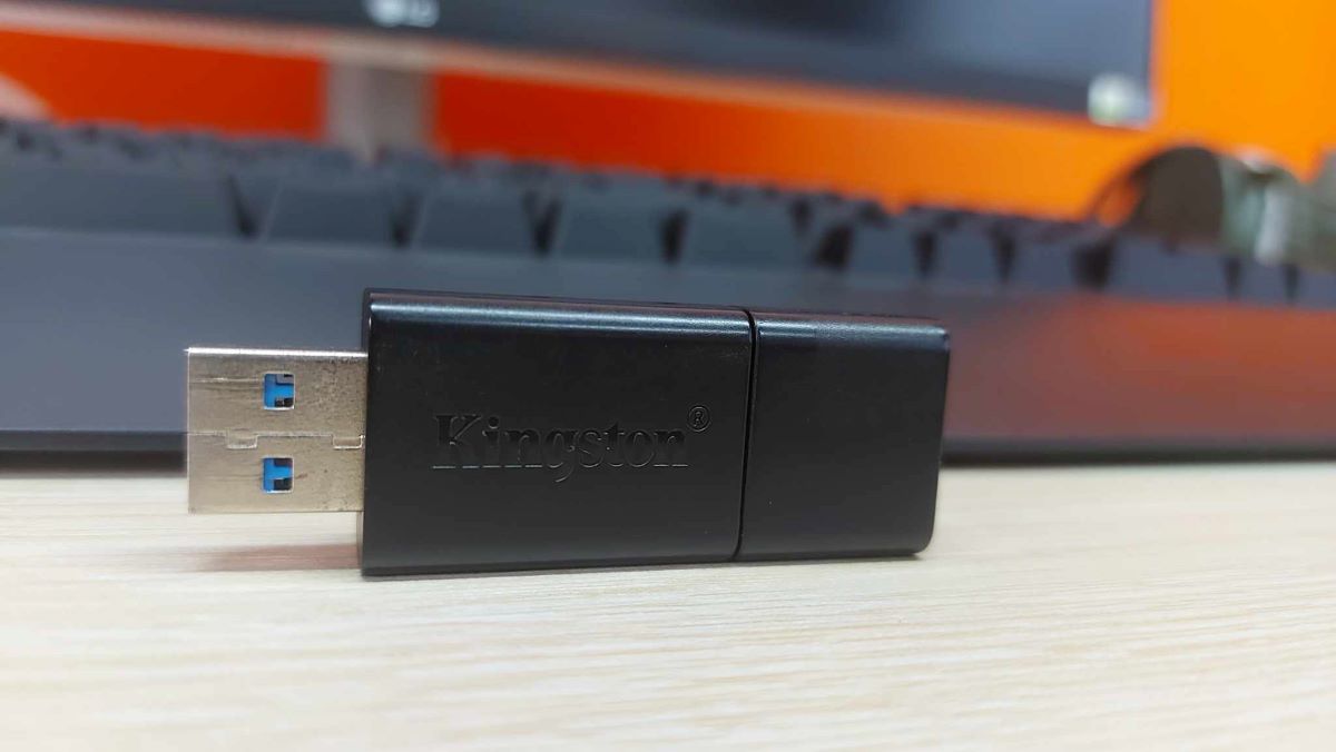 Kingston USB on a wooden table with a keyboard at the back and the orange background