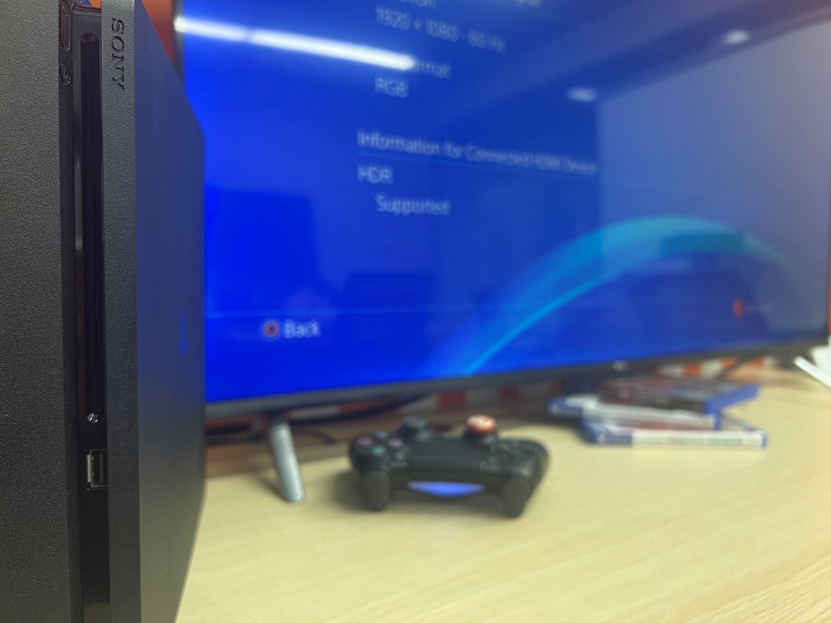 The PS4 slim and the controller is lying on a wooden table connected with a TCL TV showing HDR is supported
