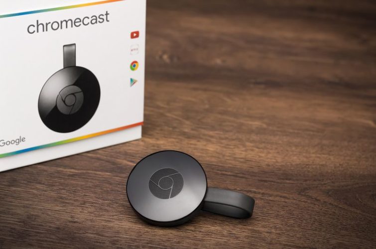 a black Google Chromecast with its original box on wooden surface
