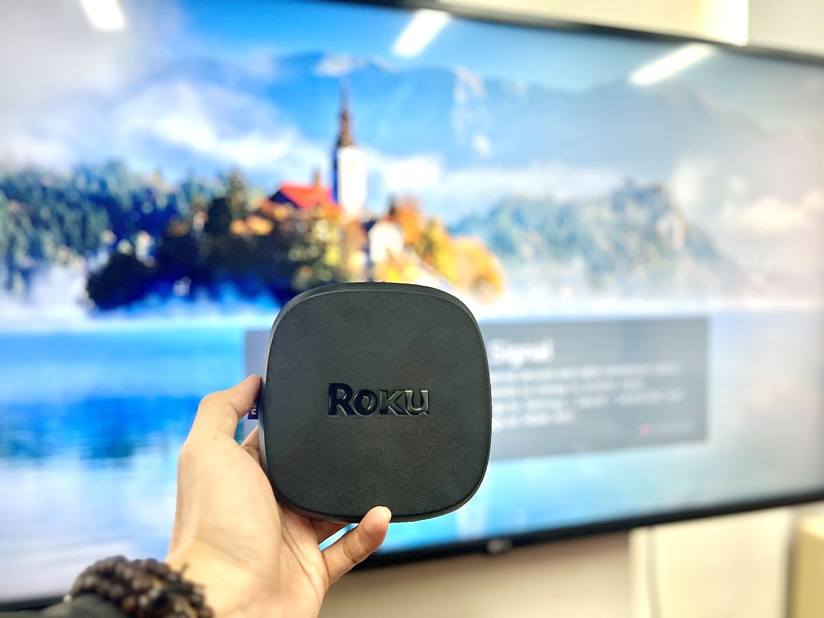 a hand holding Roku ultra in front of an LG TV