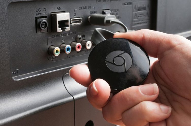 a hand holding a Chromecast connected to TV