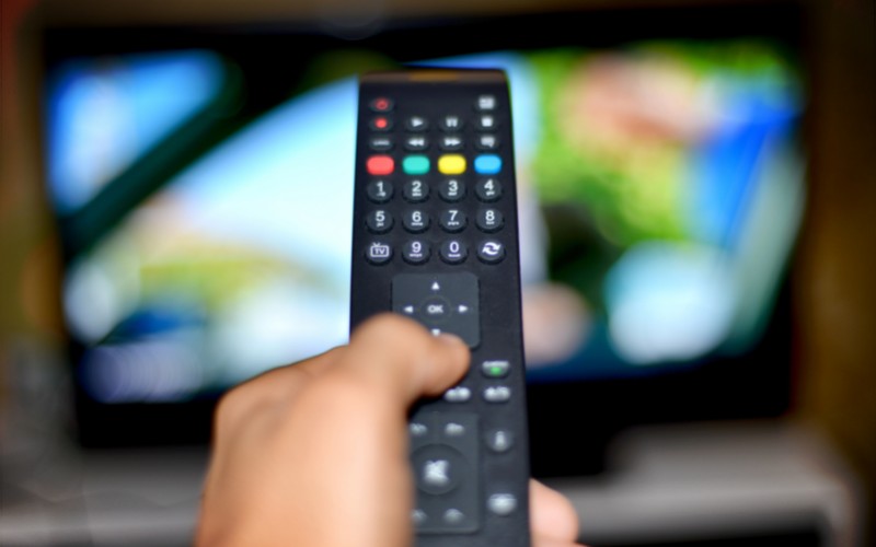 a hand holding a black remote to control the TV