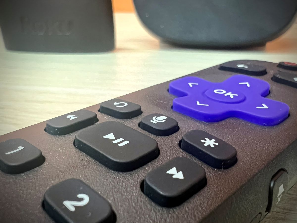 a roku remote on a table with two roku players in the background