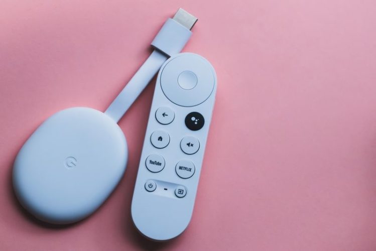 a white Google Chromecast and remote in pink background