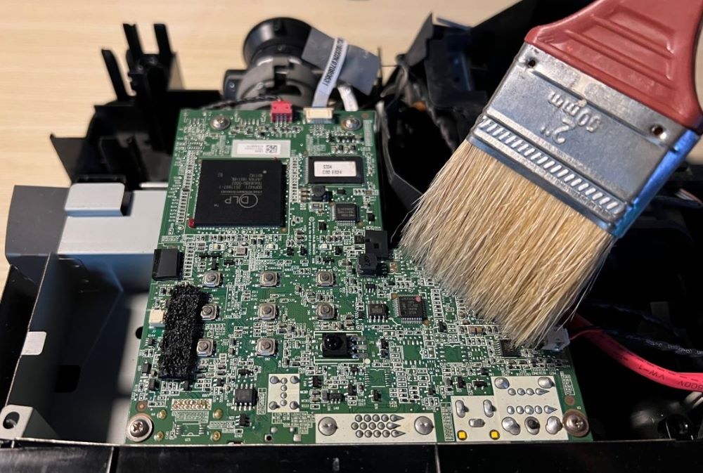 A clean painting brush is used to clean a projector motherboard