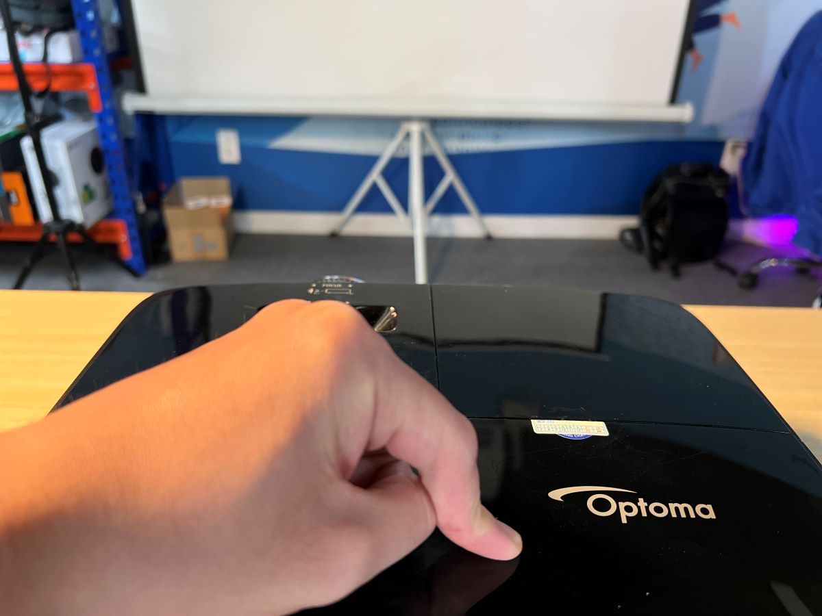 A hand is pressing on an Optoma projector hardly