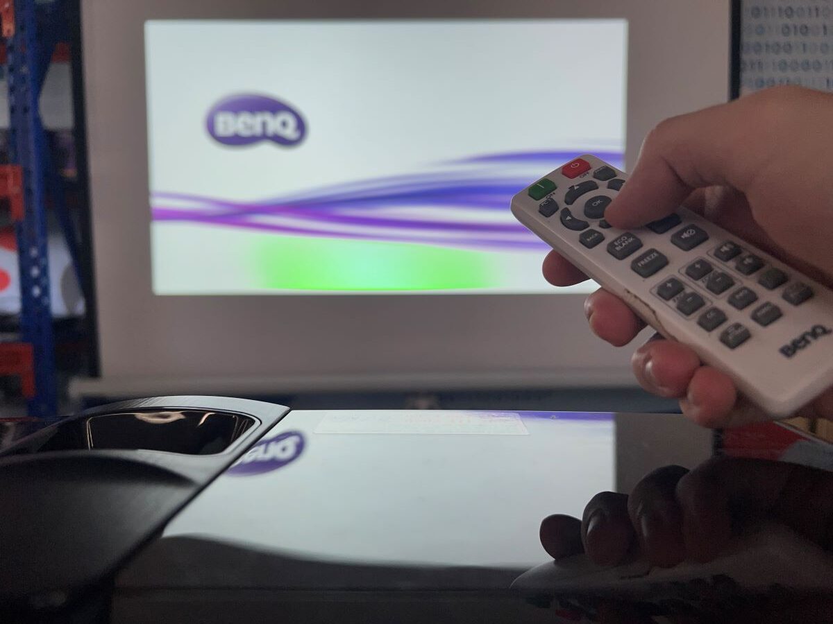 A hand is trying to control the BenQ projector using its remote but looks like the remote is not working