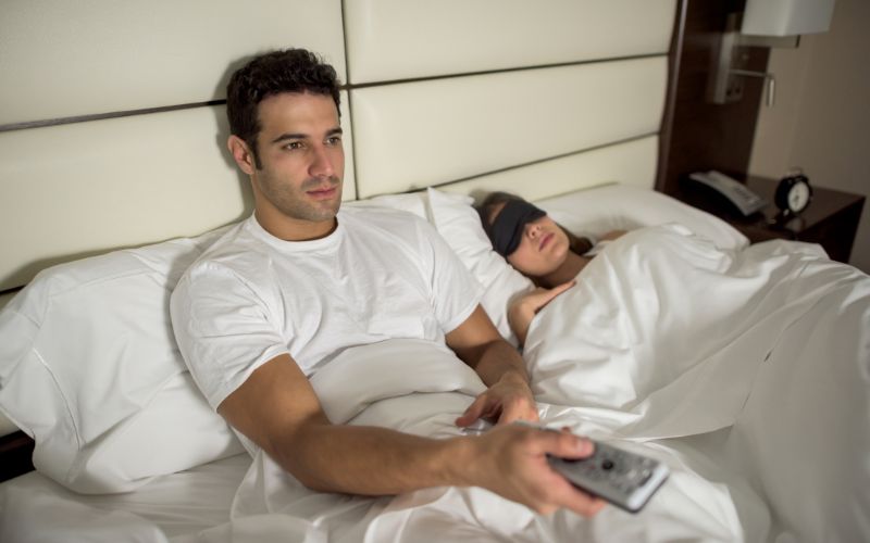 man watches TV while his wife wears sleep mask