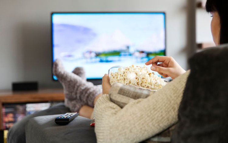 woman enjoys watching TV on the couch while eating popcorn